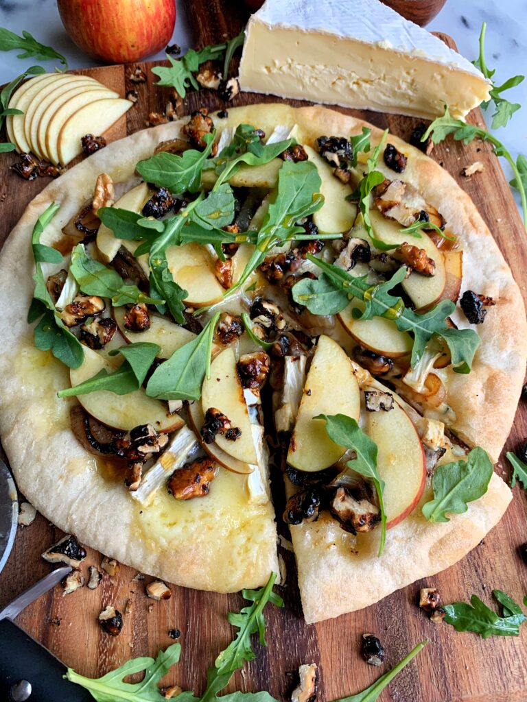 Loaded Hot Honey, Apple + Brie Pizza! A delicious flatbread pizza topped with caramelized onions, candied walnuts, arugula and the most delicious and creamy brie.